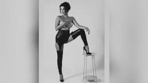 Glamorous woman in black leather leggings and high heels posing in a minimalist studio setting.