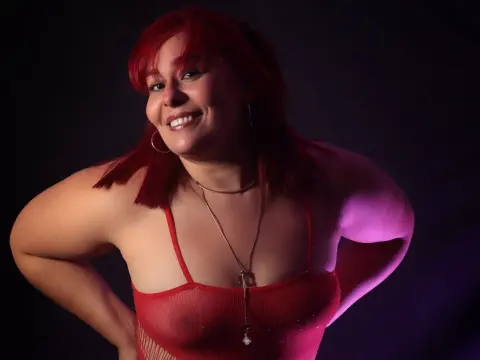 Smiling woman with red hair in a red bodysuit posing against a dark studio background.