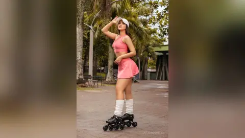 Young woman in pink athletic outfit and white visor roller skating in a sunny tropical park.
