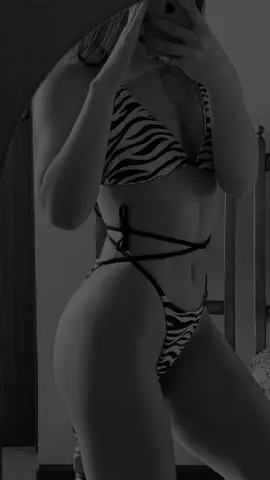 Woman in zebra print bikini posing for a mirror selfie in a moody black and white indoor setting.
