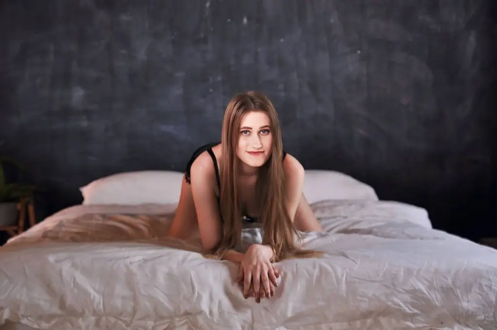Mia_Crush poses with a hand to her chin, wearing a white off-the-shoulder top and red lipstick against a white background.