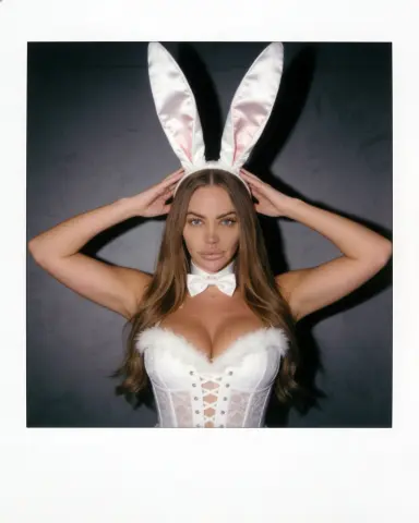 Blonde woman in white bunny ears and lace corset outfit posing against a dark studio background.
