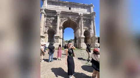 Woman in a black dress standing before the ancient Roman Arch of Constantine on a sunny day.
