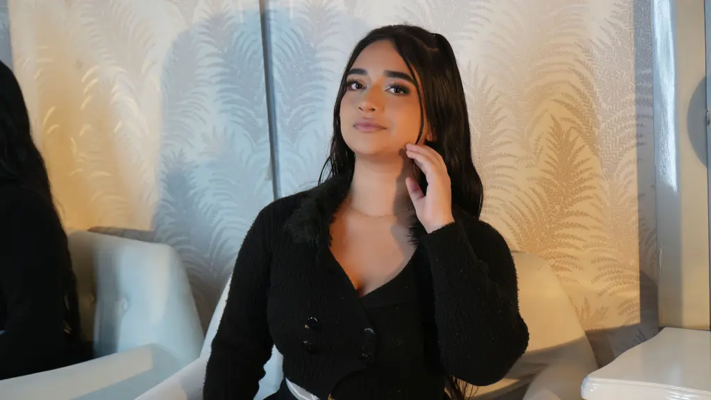 MaraBackers poses with her long dark hair, wearing a black long-sleeved top while looking toward the camera in a bright room.