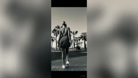Woman in a dark summer dress walking through a sunny tropical palm tree resort in black and white.