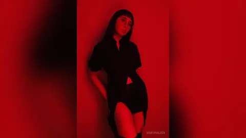 Moody portrait of a woman in a black shirt and shorts against a deep red background.