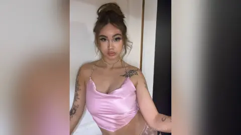 Young woman in a pink satin camisole top posing indoors with a soft, natural aesthetic.