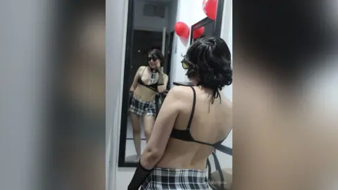 Woman in black lingerie and plaid skirt taking a mirror selfie in a room with red balloons.