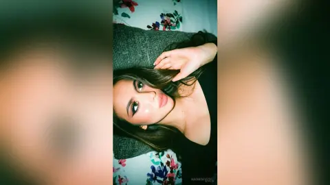 Young woman with long dark hair in a black top relaxing on a floral patterned bed with a serene expression.