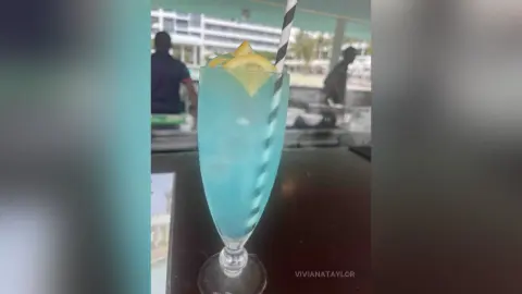 Refreshing blue tropical cocktail with lemon garnish in a tall glass on a sunny outdoor patio table.