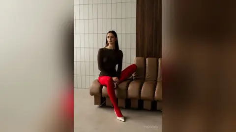 Elegant woman in a brown long-sleeve top and red leggings sitting on a modern sofa in a minimalist room.