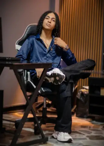 KylePresly sits in a black office chair wearing a dark blue button-down shirt and black pants.