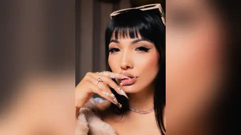 Glamorous woman with dark bangs and winged eyeliner wearing a fuzzy white outfit and sparkling jewelry.