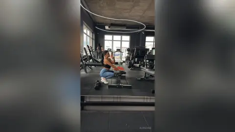 AlmaKane — Young woman in blue leggings taking a gym selfie in a modern, moody fitness studio.