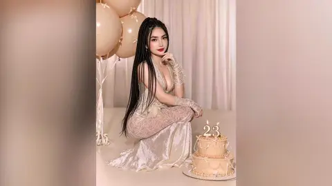 Elegant woman in white lace dress celebrating 23rd birthday with cake and balloons in a dreamy setting.