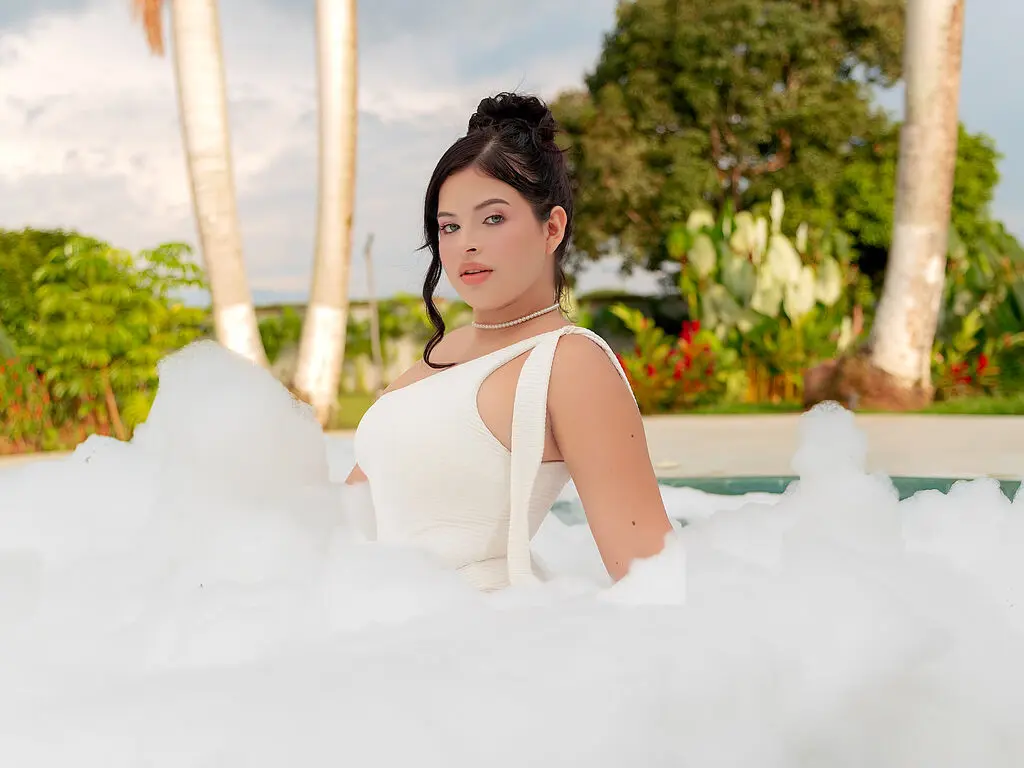 Young woman in a white dress relaxing in a dreamy bubble bath outdoors amidst tropical palm trees.
