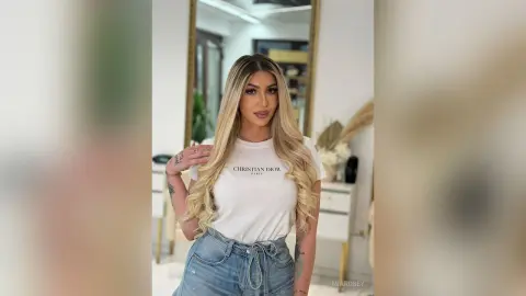 Blonde woman in a white Christian Dior t-shirt and denim jeans posing in a bright, modern minimalist room.