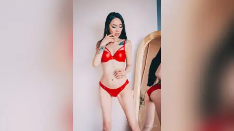 Tattooed woman in a red bikini set posing confidently in a bright minimalist room.