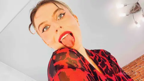 Playful woman in a red and black patterned top making a funny face in a bright indoor setting.