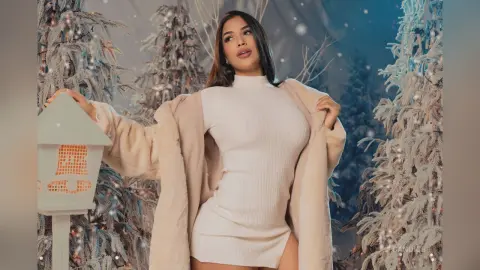 Elegant woman in a white ribbed dress and beige faux fur coat posing in a snowy winter wonderland setting.