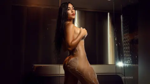 Sensual woman in sheer nude bodysuit posing in a modern elevator with moody lighting.