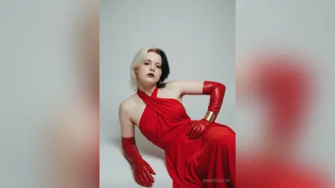 Elegant woman with split-dye hair in a glamorous red evening gown and gloves posing against a white studio backdrop.