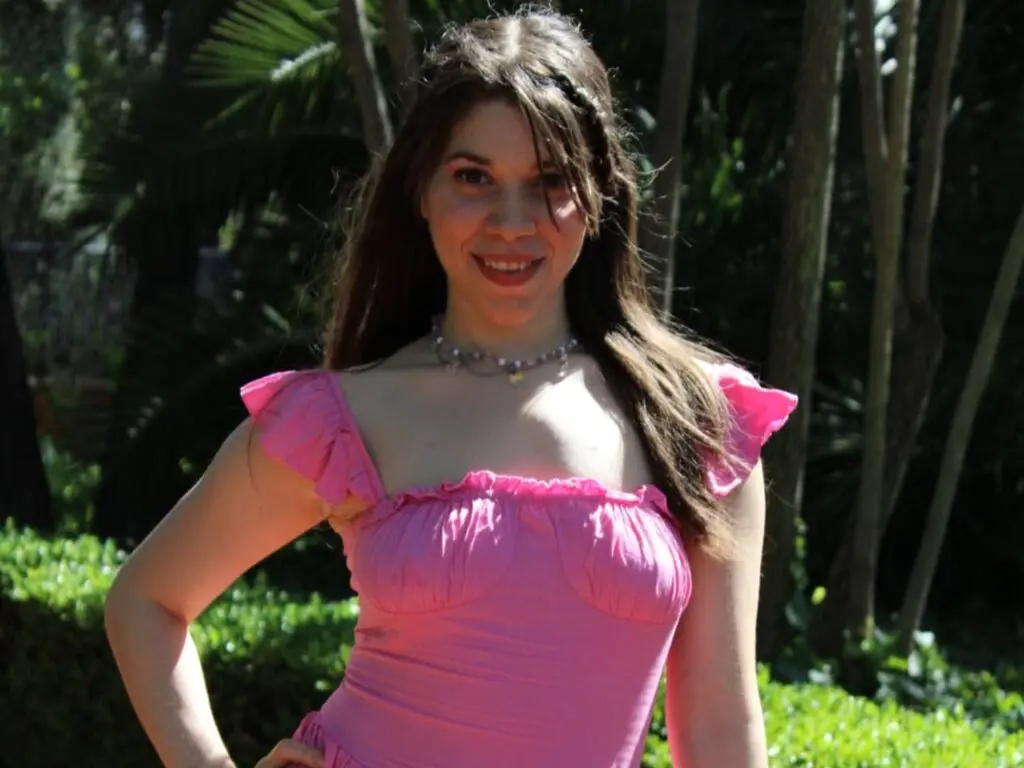 Smiling young woman in a pink summer top posing in a lush green tropical garden.