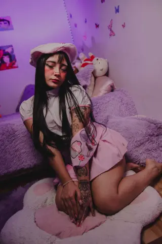 Young woman in pink aesthetic outfit and beret sitting in a cozy purple bedroom with plushies.