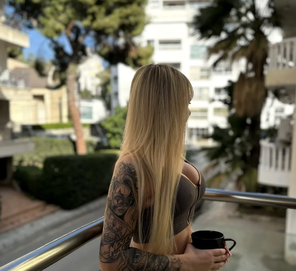 LiluDavis is a blonde woman with bangs wearing a black lace bra, posing in a gold patterned armchair.