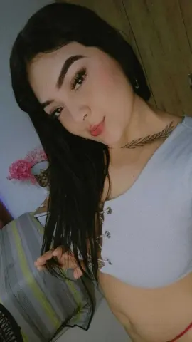 Young woman with long dark hair wearing a white crop top in a bright indoor setting.