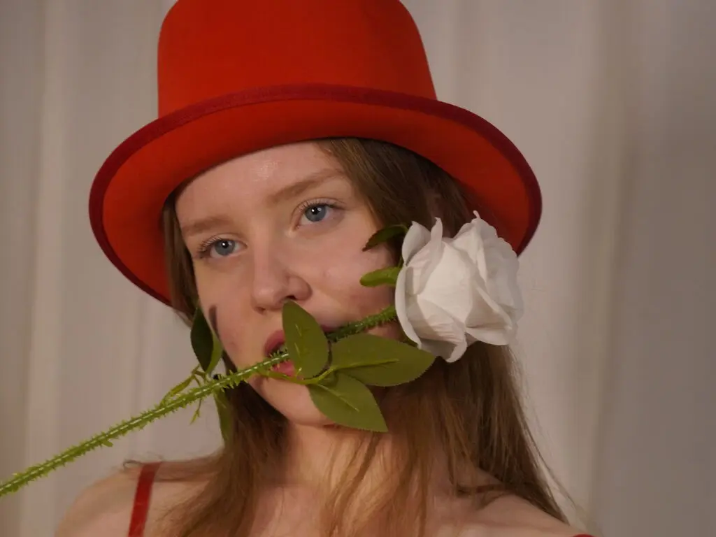 Redheaded woman in a red top hat holding a white rose for a romantic and whimsical portrait.