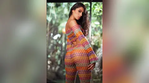 LucyMartin poses sideways in a colorful, open-knit crochet outfit that shows her skin through the mesh patterns.