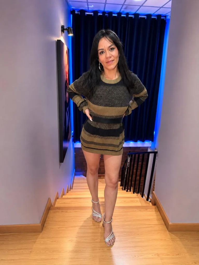 brandibae poses with a hand to her chin, wearing a white collared shirt and dark eye makeup with her dark hair pulled back.