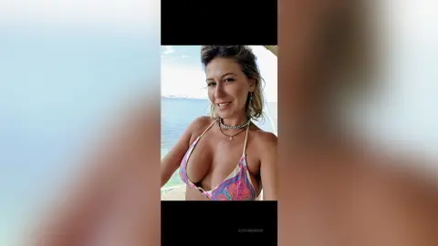 AlexiaMendoza smiles while wearing a patterned pink bikini top, showing off her cleavage against a bright ocean background.