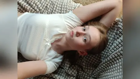Young woman in a white ribbed top relaxing on a textured blanket in a cozy, peaceful mood.