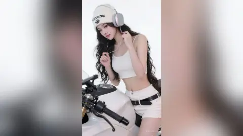 Young woman in white crop top and beanie wearing headphones while sitting on a white scooter.
