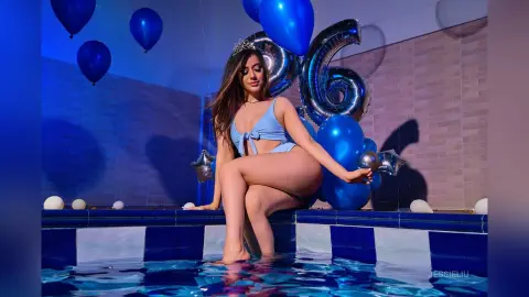 JessieLiu sits on the edge of a blue tiled pool wearing light blue bikini tops and showing her bare legs and buttocks.