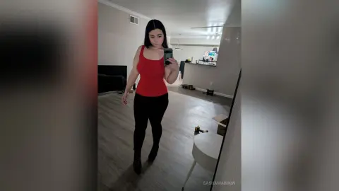 SashaMaroon stands in a room wearing a red tank top and black leggings, taking a mirror selfie.