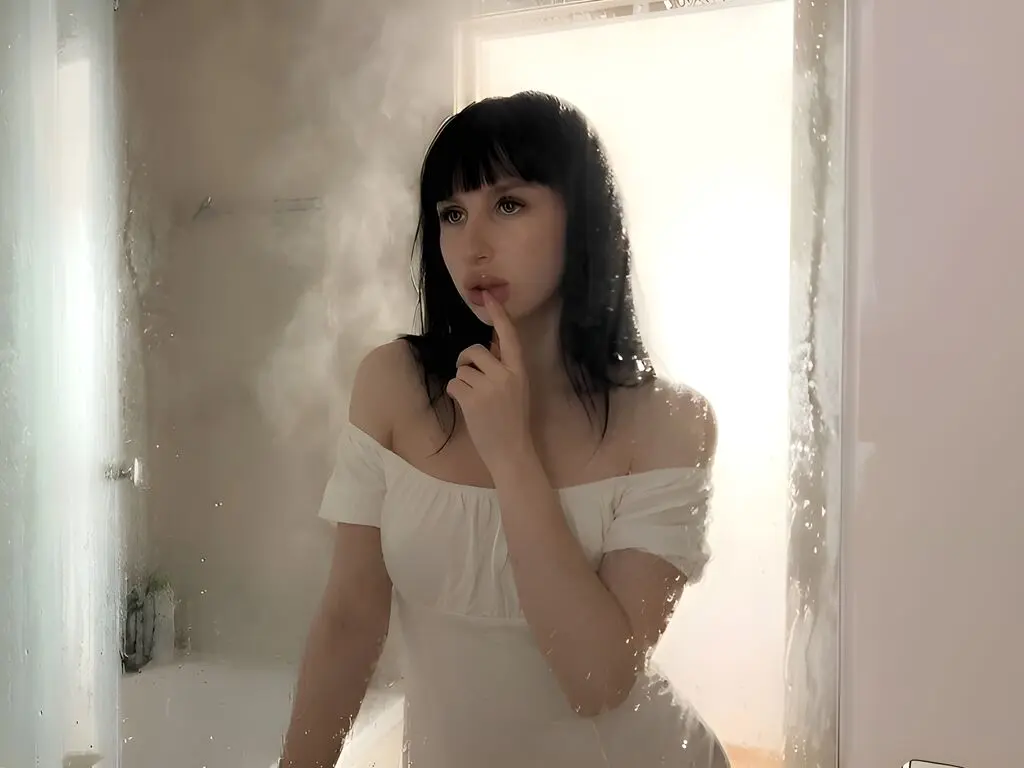 Thoughtful young woman in a white off-the-shoulder dress posing in a steamy, dreamy bathroom setting.