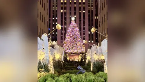 Glowing angel statues standing before a large decorated Christmas tree at Rockefeller Center at night.