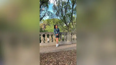 Stylish woman in a blue patterned mini dress standing by a stone balustrade in a lush green park.