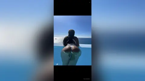 Woman in a white bikini sitting by an infinity pool overlooking the ocean under a clear blue sky.