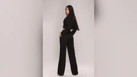 Elegant woman in a chic black long-sleeve crop top and wide-leg trousers posing against a white studio background.