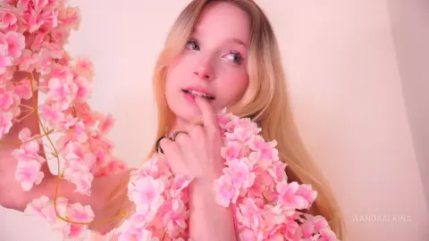 Blonde woman in a dreamy pink floral outfit posing against a soft pastel background with a romantic mood.