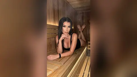 Relaxed woman in a black swimsuit relaxing in a warm wooden sauna spa setting.