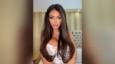 Glamorous woman with long brunette hair wearing a white satin corset in a bright, elegant indoor setting.