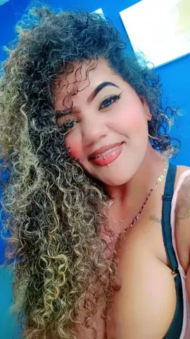 Smiling woman with long curly blonde hair wearing a black tank top against a blue background.