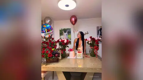 Happy woman in a white dress celebrating her birthday with red roses and a cake in a festive room.