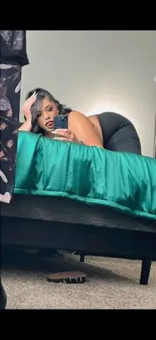Glamorous woman in a black outfit relaxing on a green bed in a cozy bedroom setting.