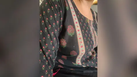 Woman wearing a black floral print long sleeve tunic in a casual indoor setting.